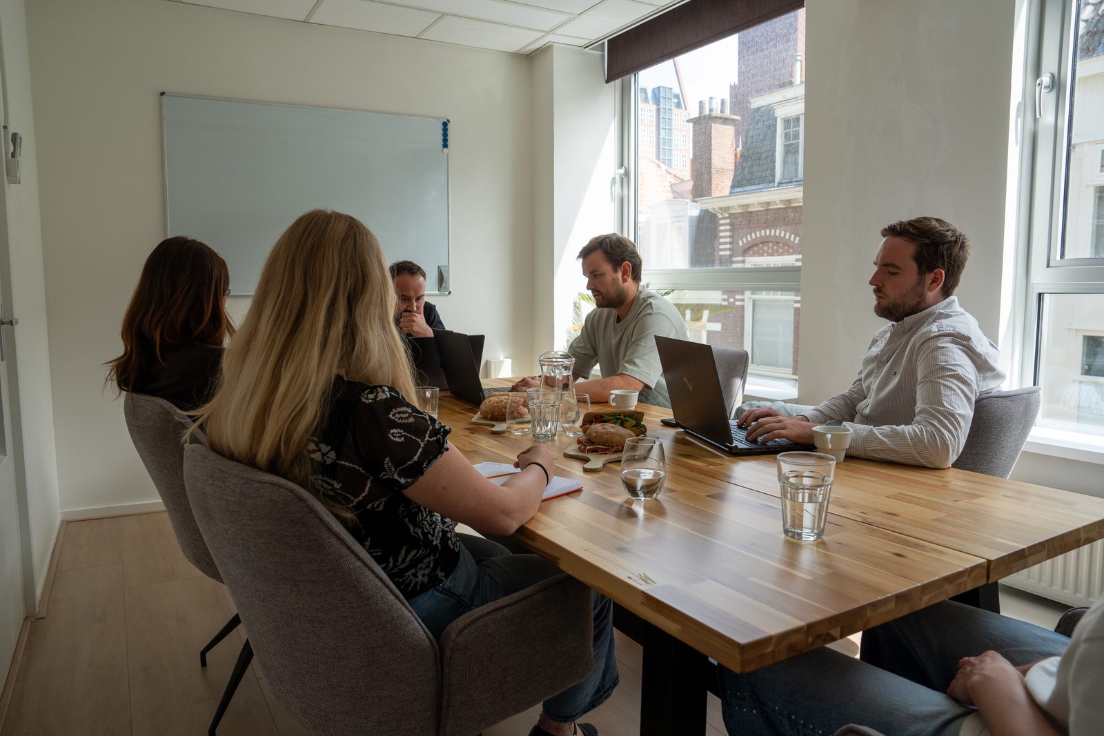 Team rond een lange vergadertafel met laptops in een lichte kantoorruimte