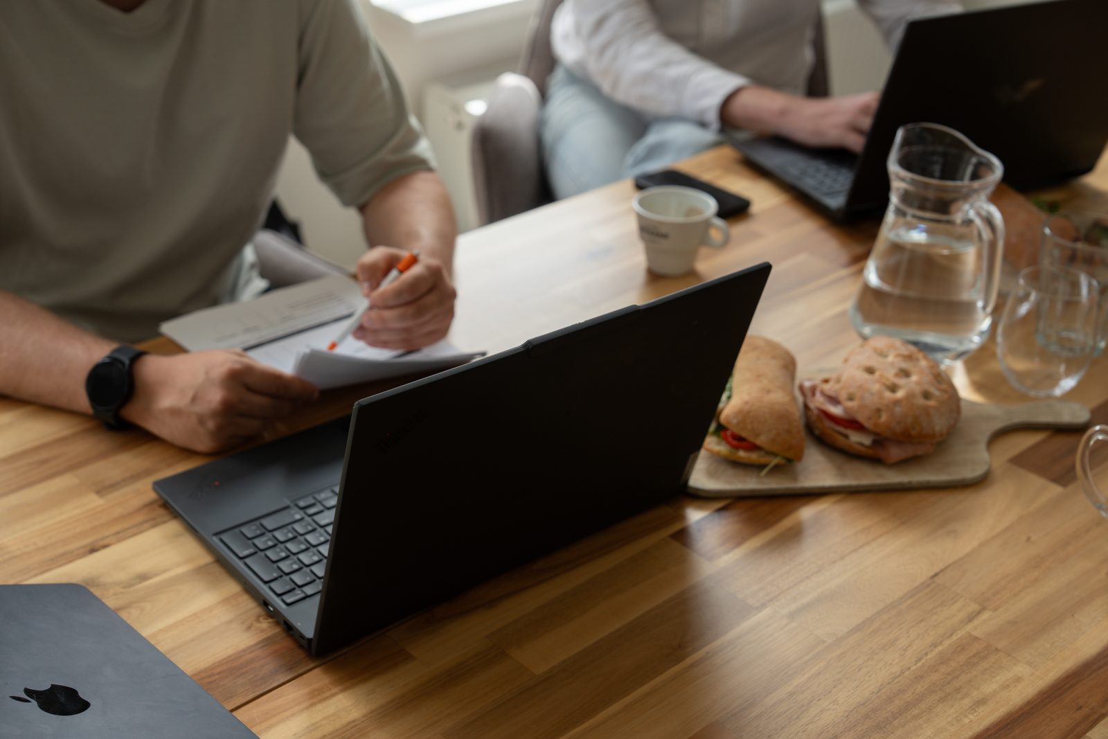 Laptop op een houten vergadertafel met broodjes en een waterkaraf tijdens een werksessie